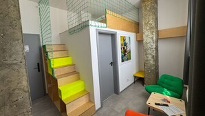 Ein kompakter Wohnraum mit einer Holztreppe, einer kleinen Sitzecke mit Tisch und einer Tür mit farbenfroher Kunst.