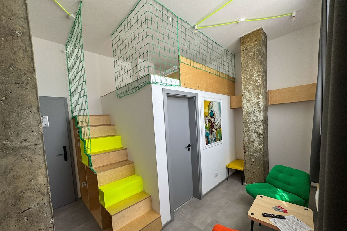 Ein kompakter Wohnraum mit einer Holztreppe, einer kleinen Sitzecke mit Tisch und einer Tür mit farbenfroher Kunst.