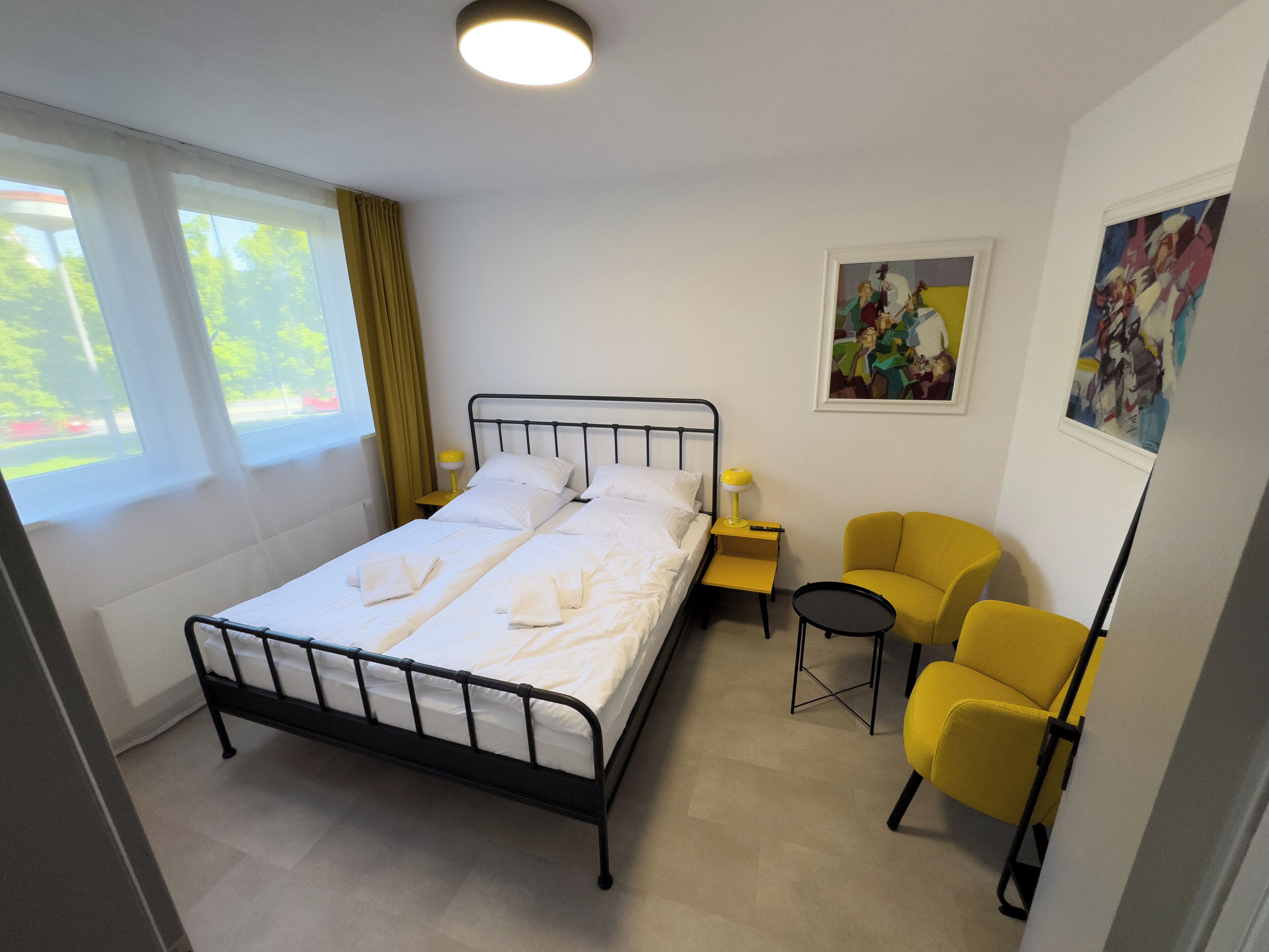 Een hotelkamer met een bed, een tafeltje, twee stoelen en kunstwerken aan de muur.