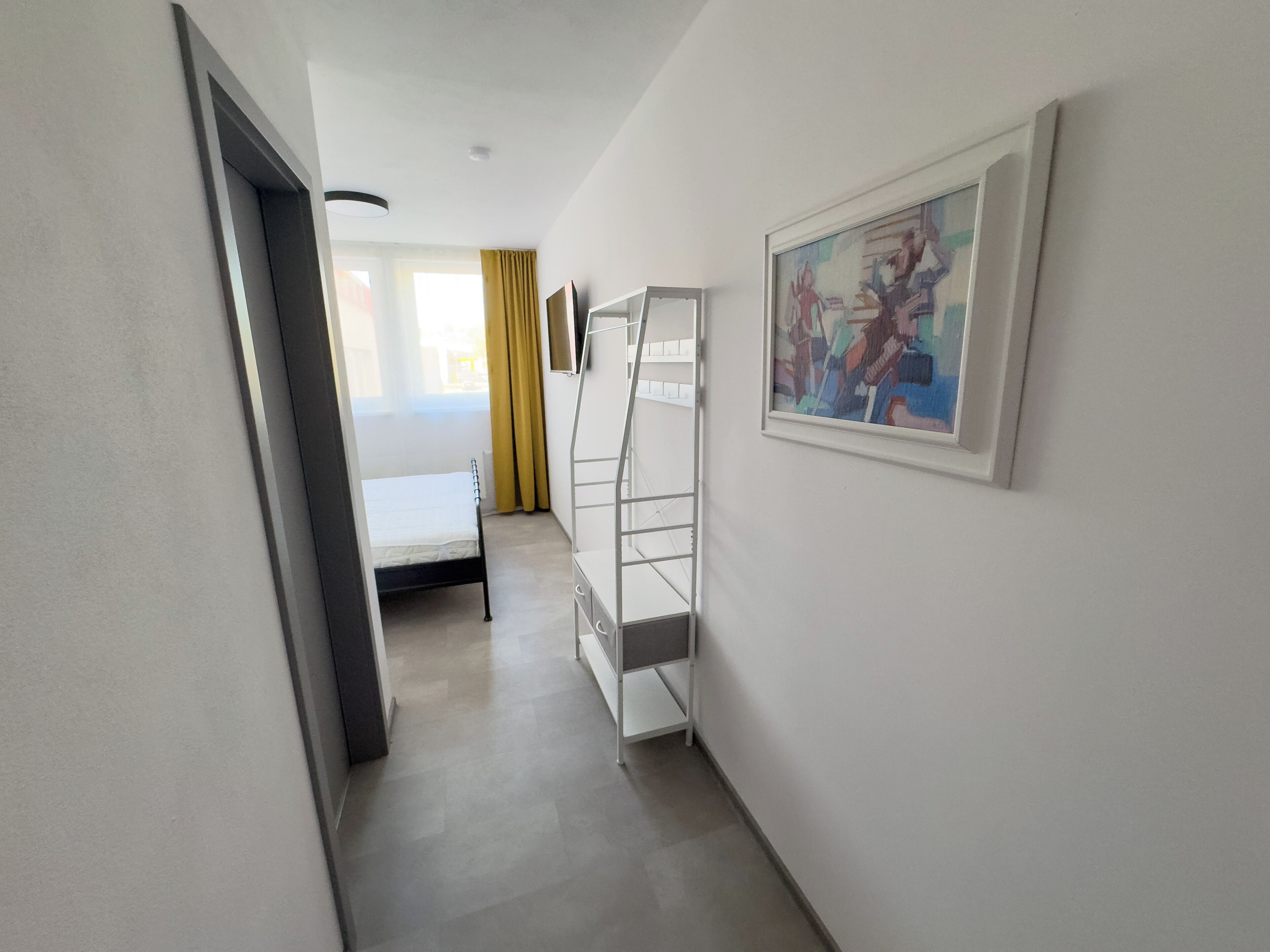 A narrow hallway with a bed, a white dresser, and a painting on the wall.