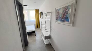 A narrow hallway with a bed, a white dresser, and a painting on the wall.