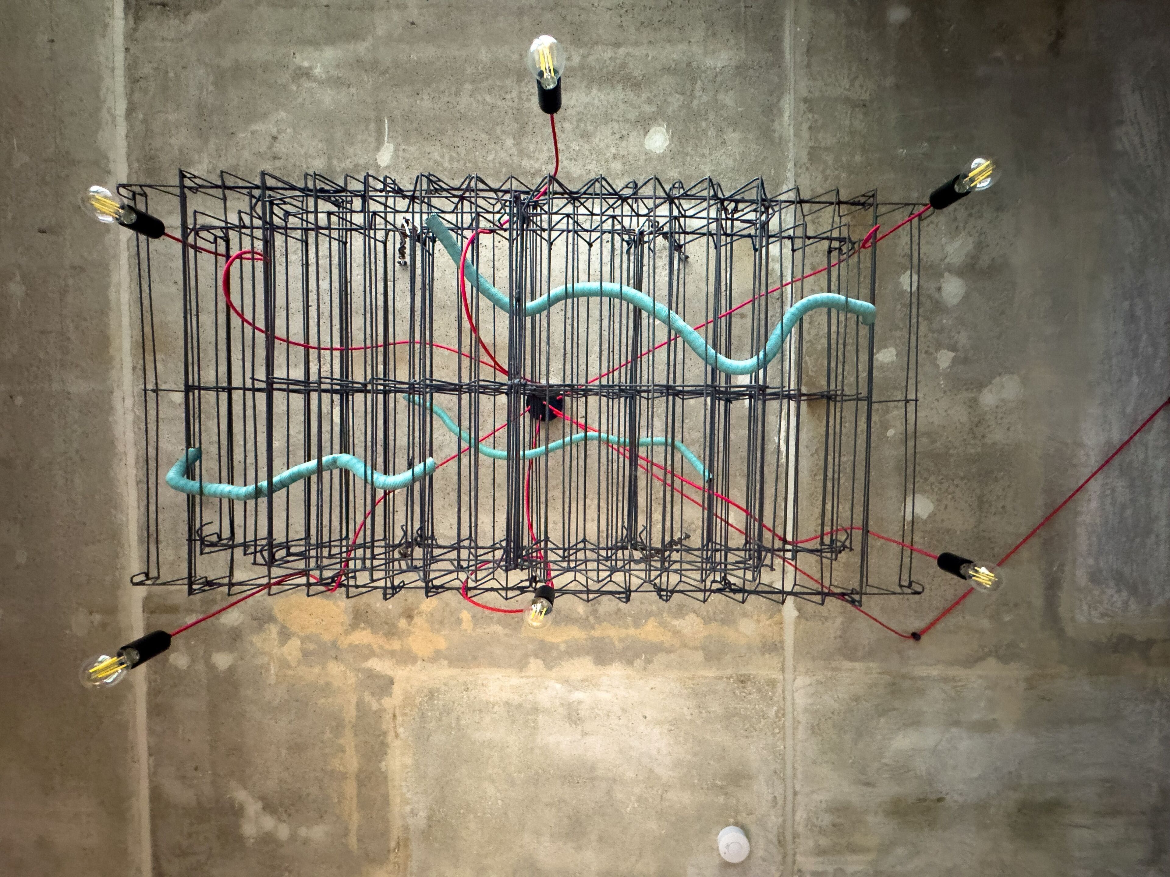 Una estructura metálica con cables y bombillas frente a un muro de concreto.