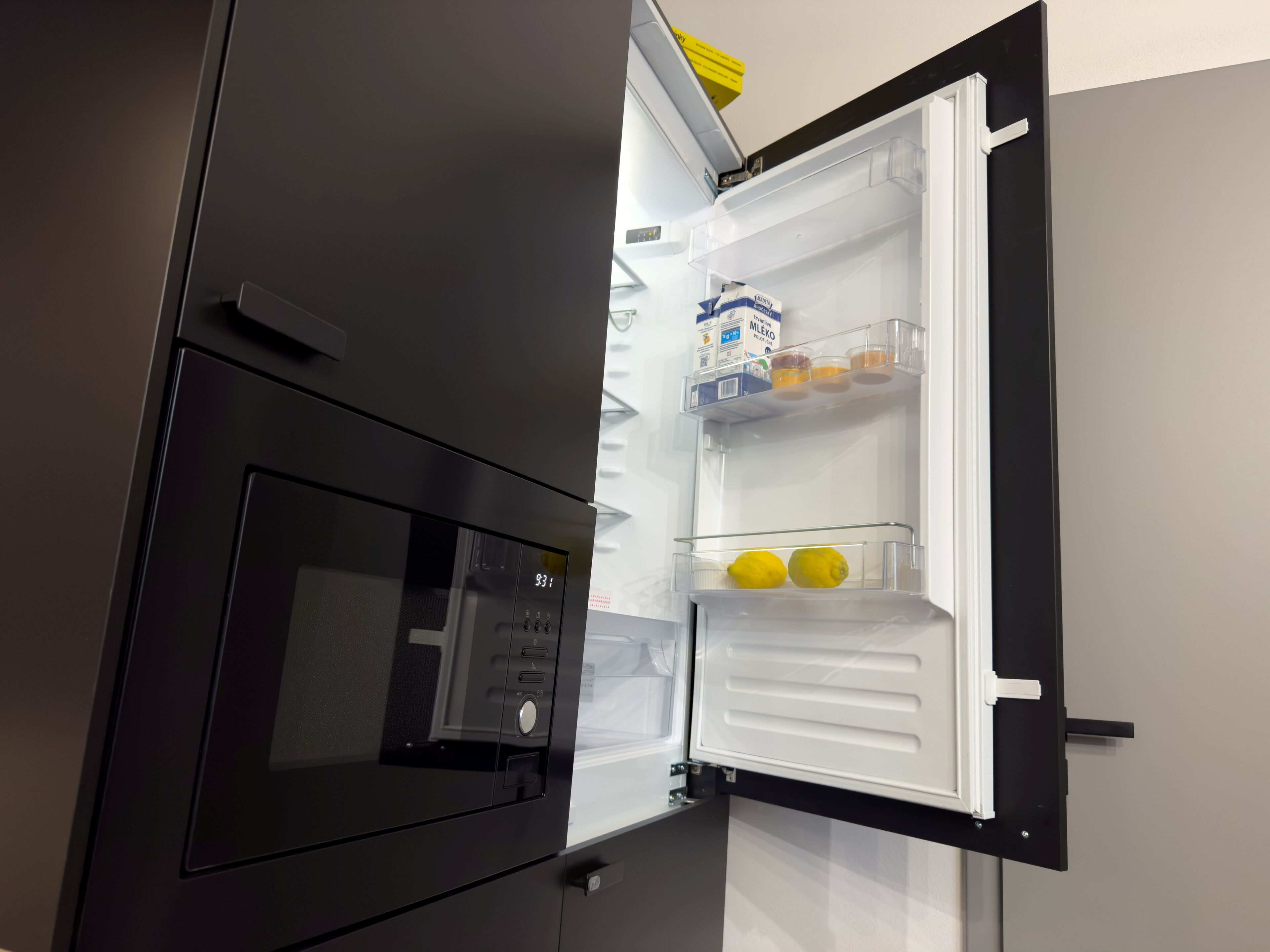 Een moderne keuken met een ingebouwde magnetron en een koelkast met heldere planken.