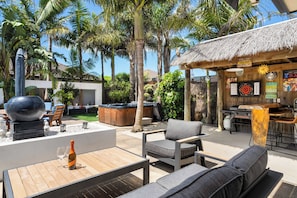 Un espacio de patio al aire libre con asientos, un jacuzzi y una zona de bar con techo de paja.