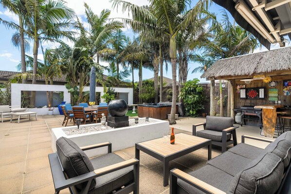 Un patio exterior con mobiliario moderno, zona de barbacoa y exuberante vegetación tropical.