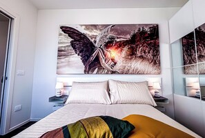 A bedroom with a large bed, two bedside tables with lamps, and a large painting of an angel on the wall.