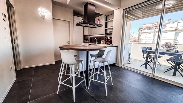A modern kitchen with a central island, white bar stools, and a large sliding glass door leading to an outdoor dining area. - Saxony, close to the Center and the Sea Cozy new apartment (Fano)