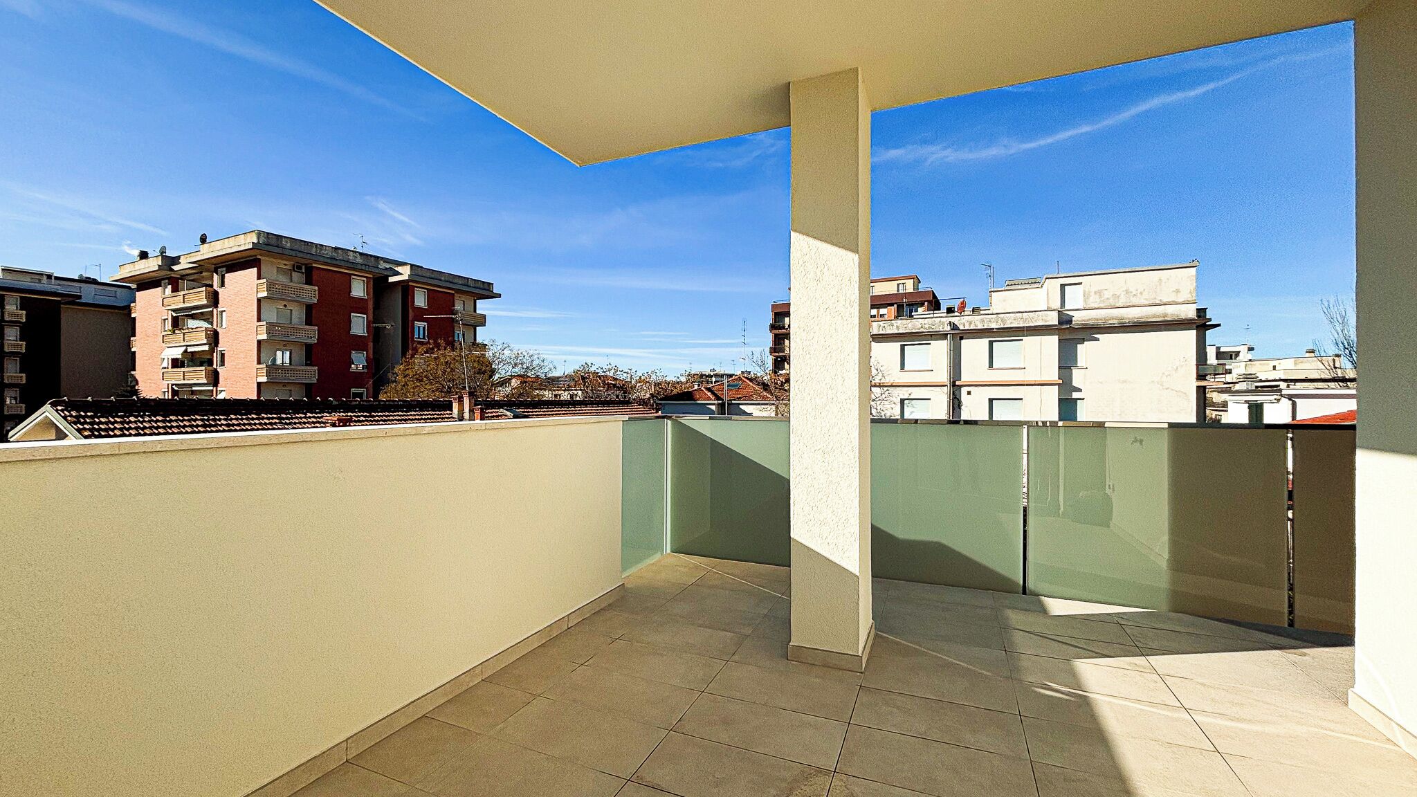 A balcony with a tiled floor and a view of surrounding buildings.