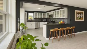 Une cuisine moderne avec des meubles blancs, un plan de travail noir et un îlot central doté de tabourets de bar.