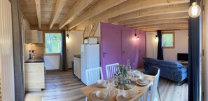 Ein gemütliches Cabin-Interieur mit Essbereich, gedecktem Tisch und einer Küche inklusive Kühlschrank, sowie einem blauen Sofa.