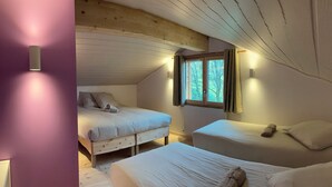 Un chalet confortable, composé d’une seule pièce, avec deux lits, une fenêtre avec des rideaux et des lampes fixées au mur.
