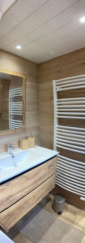 Ein modernes Badezimmer mit einem Holzwaschtisch, einem großen Spiegel, einer weißen Spüle und einem Handtuchhalter.