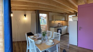 Un chalet en bois accueillant, avec un coin repas aménagé pour quatre personnes, une cuisine équipée d’appareils modernes et une porte violette.