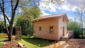 Une cabane en bois avec un toit en tuiles, une terrasse en bois et un petit escalier menant à l’entrée.