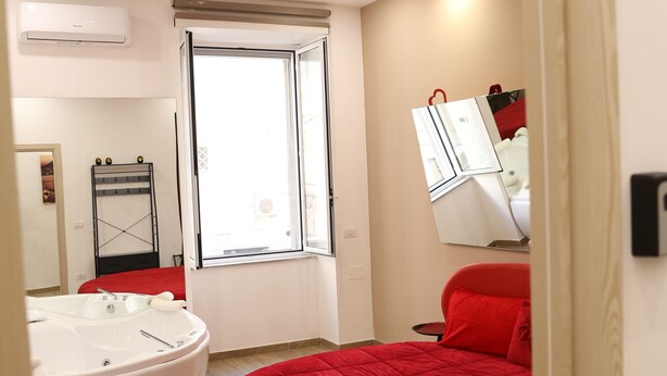 Un dormitorio moderno con una cama roja, un espejo grande y una ventana.