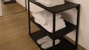 Un estante de metal negro con toallas blancas dobladas, un cuadro enmarcado arriba y un espejo en la pared.