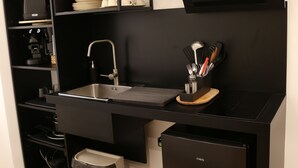 Una cocina compacta con cubierta negra, un lavamanos, una estufa integrada y un refrigerador pequeño.