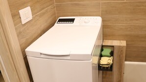 Una lavadora blanca de carga frontal, compacta, en un baño con suelo y mueble de madera.