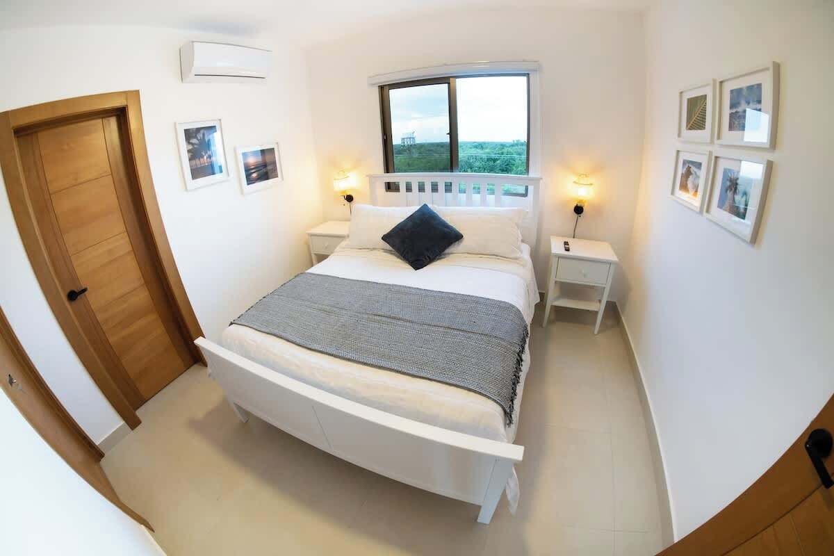 Un dormitorio con cama, lámparas de noche, una ventana y una puerta.