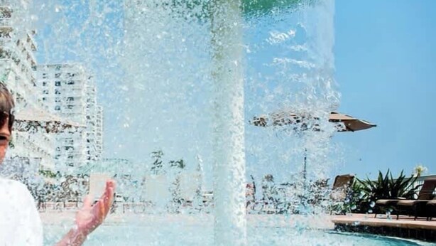 A person standing by a water fountain with a pool in the background. - Beachfront studio w/pool & fire pit (Daytona Beach)