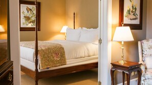 A four-poster bed with a floral bedspread, a bedside table with a lamp, and a chair with floral upholstery.