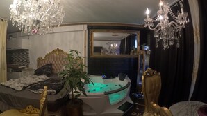 A luxurious bedroom with a large bed, a sitting area with a chair, a bathtub with lights, and a chandelier. - Hourly hotel BlackKingdom (Freiburg im Breisgau)