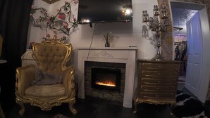 A living room with a fireplace, a television mounted above it, and a decorative candelabra. - Hourly hotel BlackKingdom (Freiburg im Breisgau)