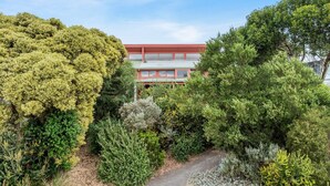 A building with a red roof and large windows, surrounded by dense greenery and a gravel path. - The Chance - Immerse yourself in the oceanic ambience of South Beach. (Port Fairy)