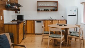 A compact kitchen with wooden cabinets, a built-in dishwasher, and a dining area with a round table and chairs. - The Chance - Immerse yourself in the oceanic ambience of South Beach. (Port Fairy)