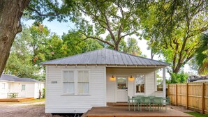 Une petite maison blanche avec un porche, le numéro 3208, et une terrasse avec des chaises vertes.