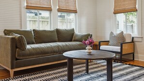 Un salon avec un canapé vert, une table basse ronde et un fauteuil en osier.