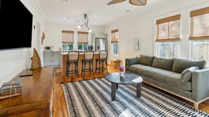 Un vaste espace de vie comprenant un canapé, une table basse et un coin repas avec des chaises, ainsi qu’une cuisine en arrière-plan.