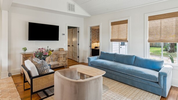 Ein Wohnzimmer mit blauem Sofa, weißem Sessel, Couchtisch aus Holz und einem flachbildfernseher an der Wand.