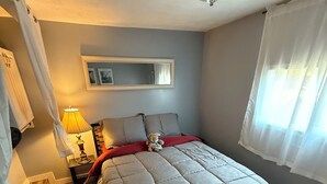 A bedroom with a bed, a nightstand, a lamp, a teddy bear, a mirror, and a window with curtains. - 
Welcome to the your budget friendly  stop right off the highway 27. (Somerset)
