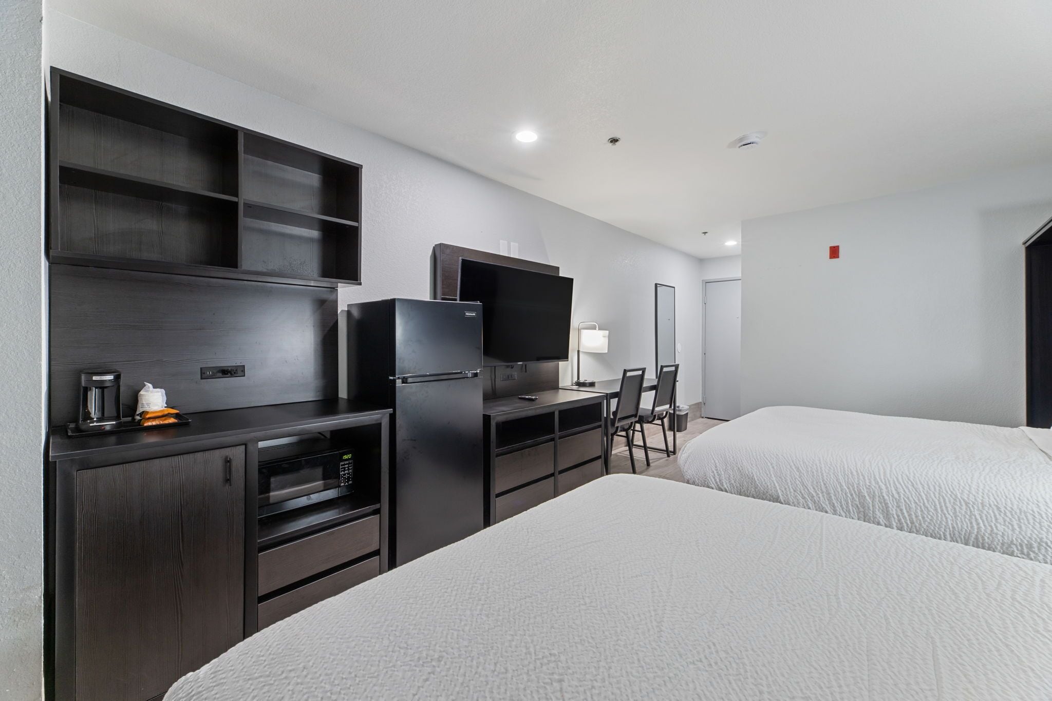 Habitación de hotel con cama, escritorio, televisión de pantalla plana, microondas, cafetera y una silla.