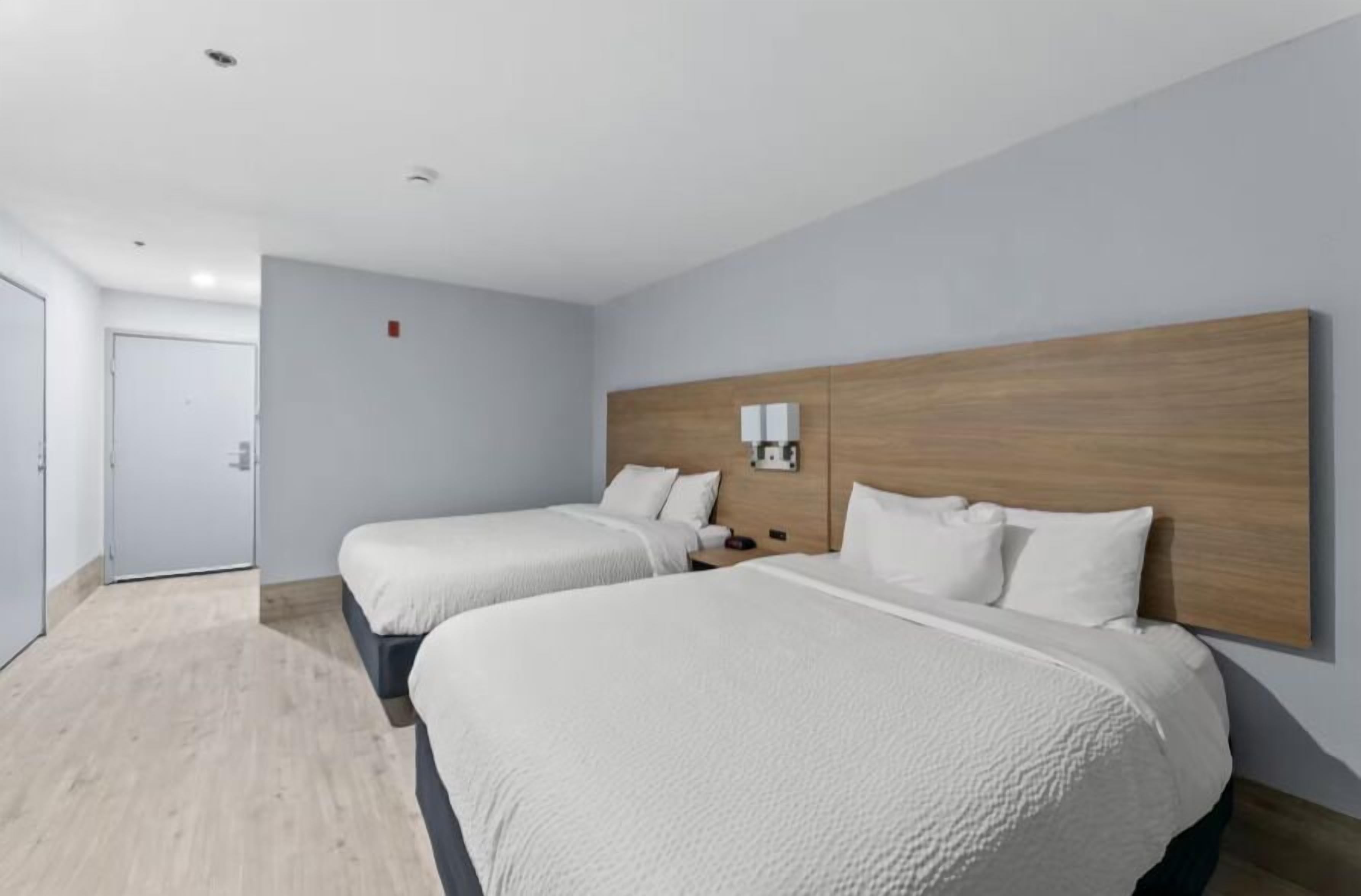A hotel room with two beds, a wooden headboard, a bedside table, and a wall-mounted light.