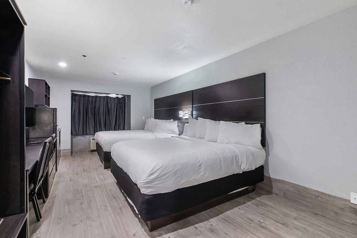 Quarto de hotel moderno com duas camas, uma escrivaninha e uma televisão.