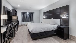Een moderne hotelkamer met een groot bed, een bureau met stoelen, een televisie en een raam met gordijnen.