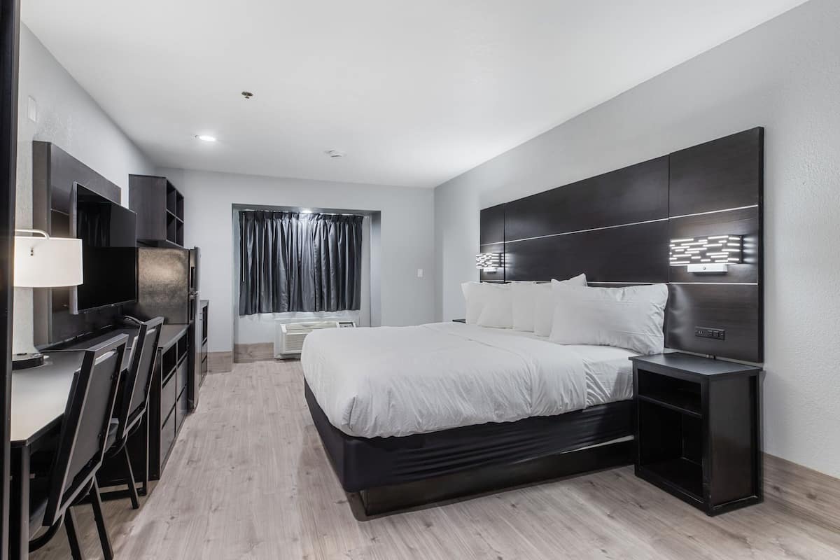 Quarto de hotel moderno com uma cama grande, uma escrivaninha com cadeiras, uma televisão e uma janela com cortinas.