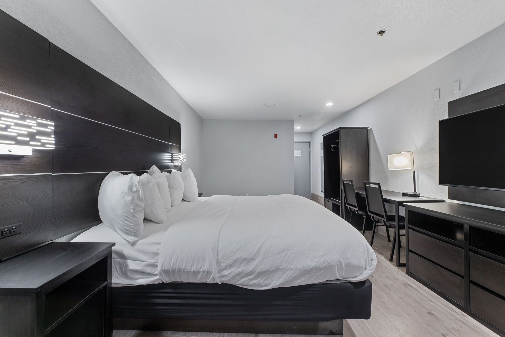 Une chambre d’hôtel moderne dotée d’un grand lit, d’un bureau, d’un téléviseur à écran plat et d’un téléviseur fixé au mur.
