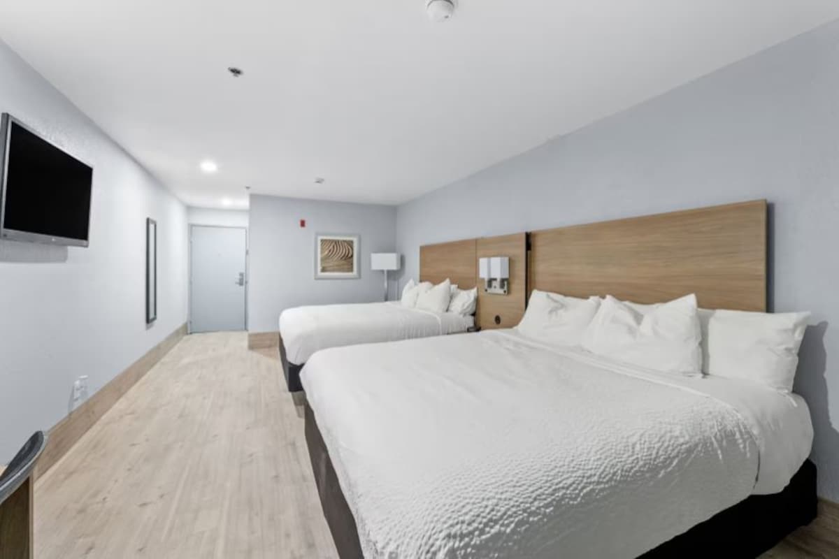 A hotel room with two beds, a flat-screen TV, a wooden headboard, and a small bedside table with a lamp.