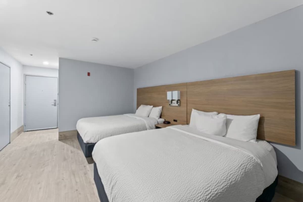 A hotel room with two beds, a wooden headboard, a bedside table, and a wall-mounted light.