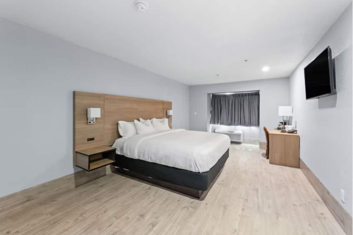 Quarto de hotel moderno com cabeceira de madeira, uma cama grande, uma escrivaninha e uma televisão de tela plana.