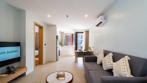 A modern living room with a flat-screen TV, a sofa, a coffee table, and a kitchen area in the background. - Wyndham Garden Samui Wing (Koh Samui)