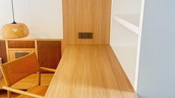 Una mesa de madera sencilla con una silla, una lámpara de fibras tejidas y un enchufe en la pared.