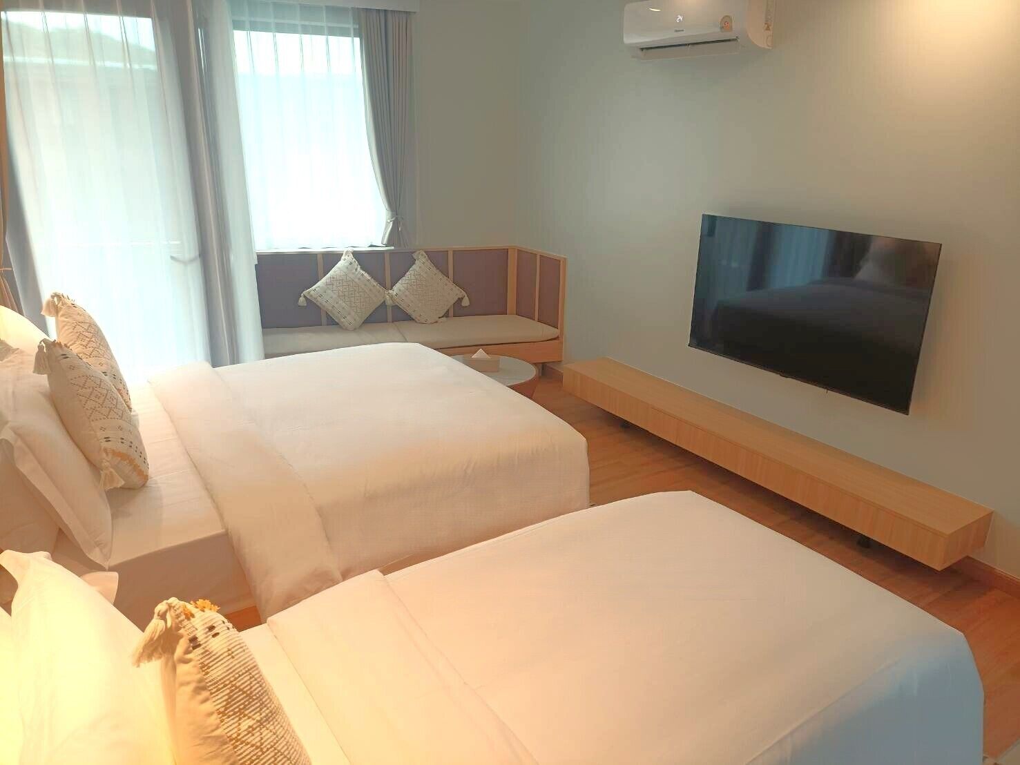 Une chambre d’hôtel avec deux lits, un téléviseur fixé au mur et une fenêtre avec des rideaux.