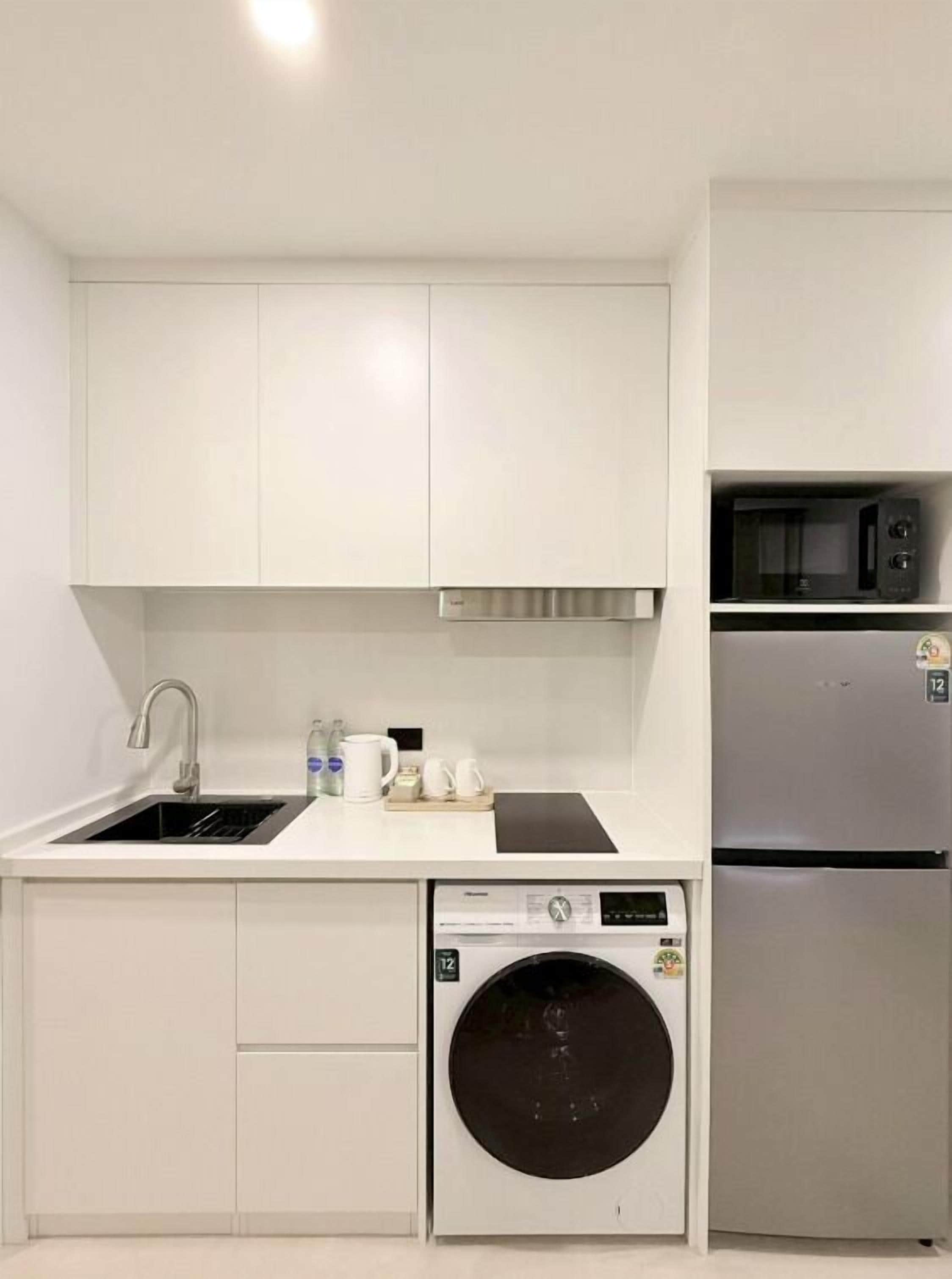 A compact kitchen with white cabinetry, a stainless steel sink, a microwave, a refrigerator, and a front-loading washing machine.