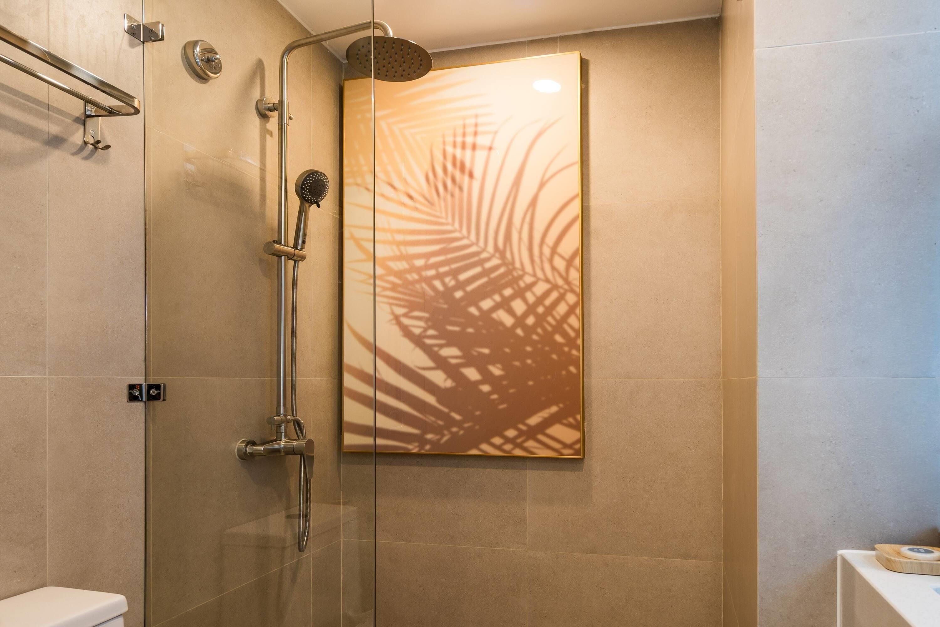 A modern bathroom with a glass shower enclosure, a handrail, and a wall-mounted artwork.