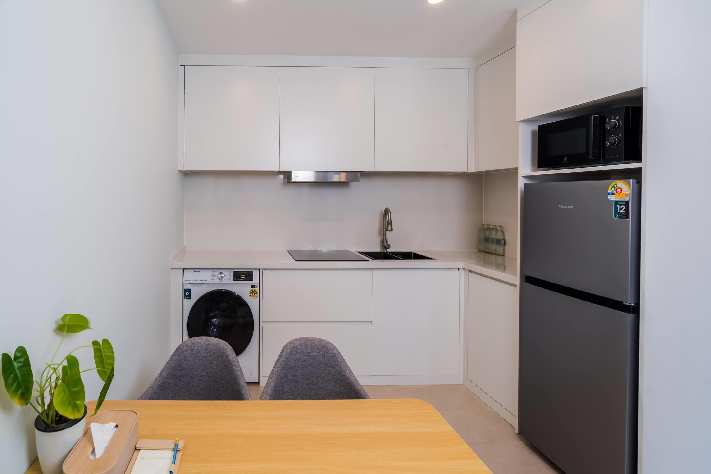Une cuisine moderne avec des meubles blancs, un réfrigérateur en acier inoxydable, un four à micro-ondes et un lave-linge.