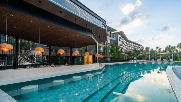 A modern hotel with a large pool, outdoor seating, and a covered area with hanging lights. - Wyndham Garden Samui Wing (Koh Samui)
